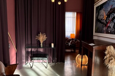 Grand arbre en pot éclairé par une lumière verte dans un salon moderne avec canapé, tables et vases de fleurs.