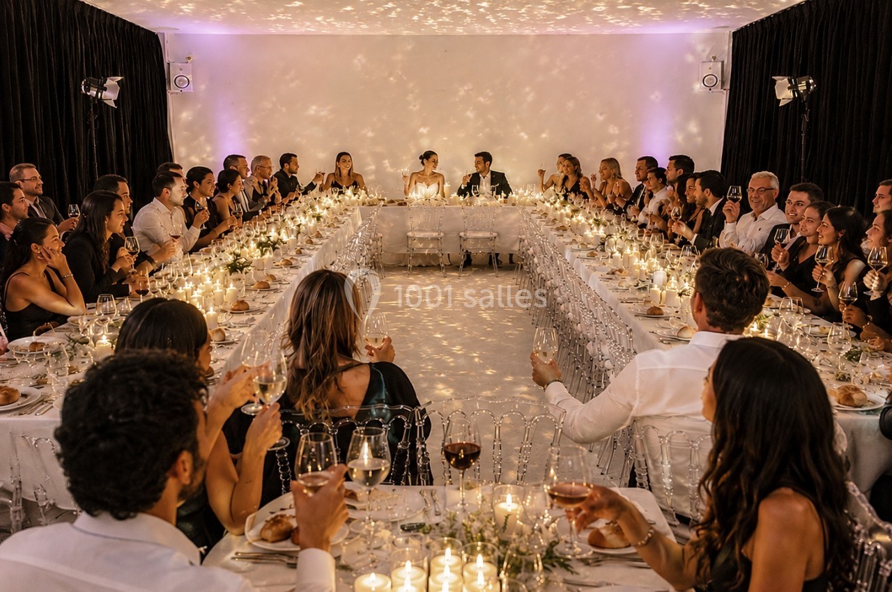 Salle de réception éclairée par des bougies, avec des invités assis autour de longues tables en U.
