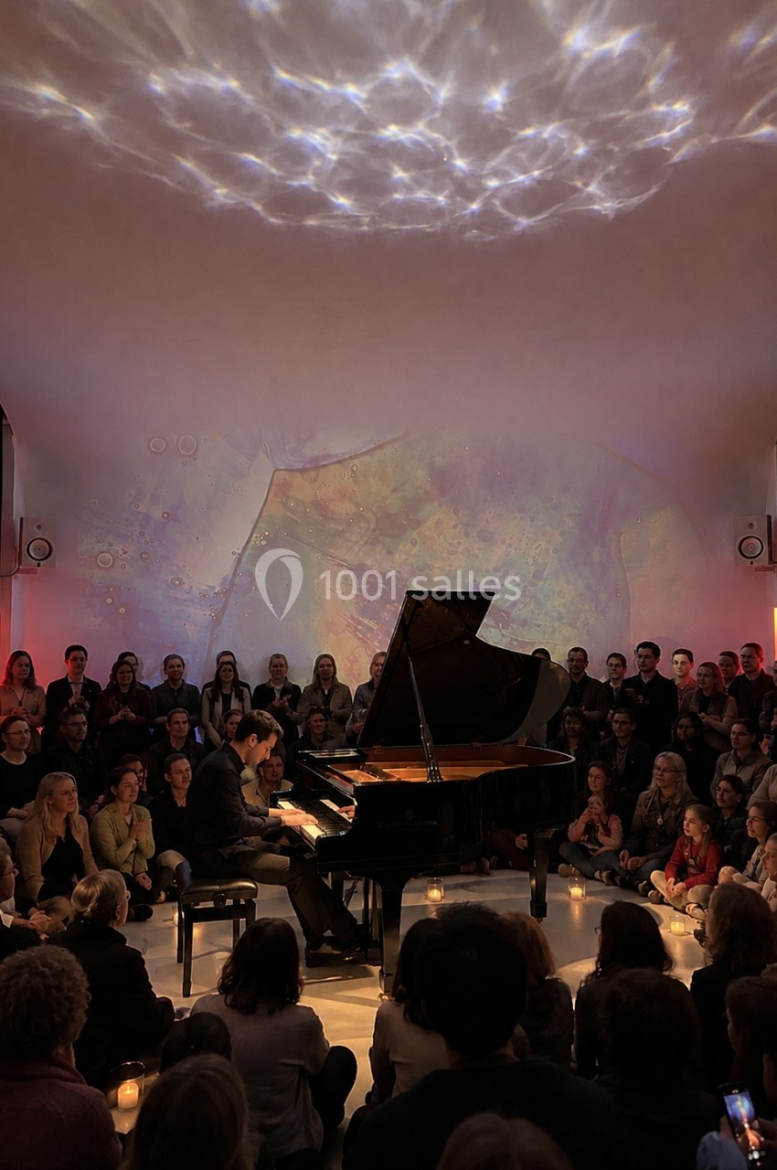 Un pianiste joue sur un piano à queue devant un public assis dans une salle à l'éclairage tamisé.