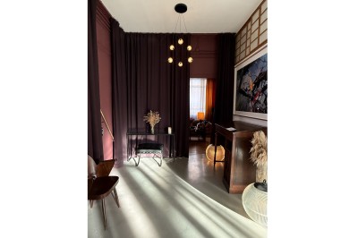 Une chaise en bois et un mannequin près d'une porte ouverte donnant sur un couloir lumineux avec une rambarde en fer forgé.