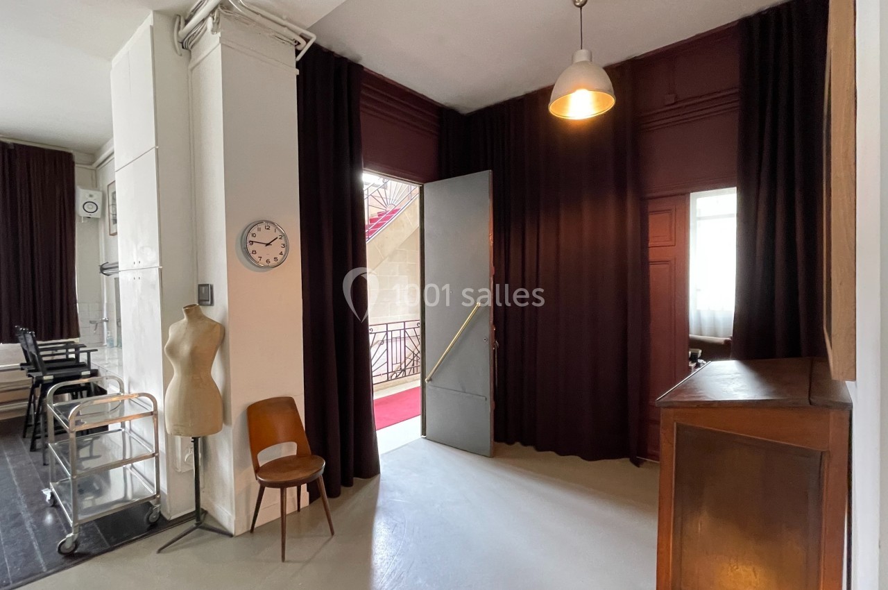 Espace intérieur avec un mannequin de couture, une chaise, un meuble en bois et une porte ouverte sur un escalier.