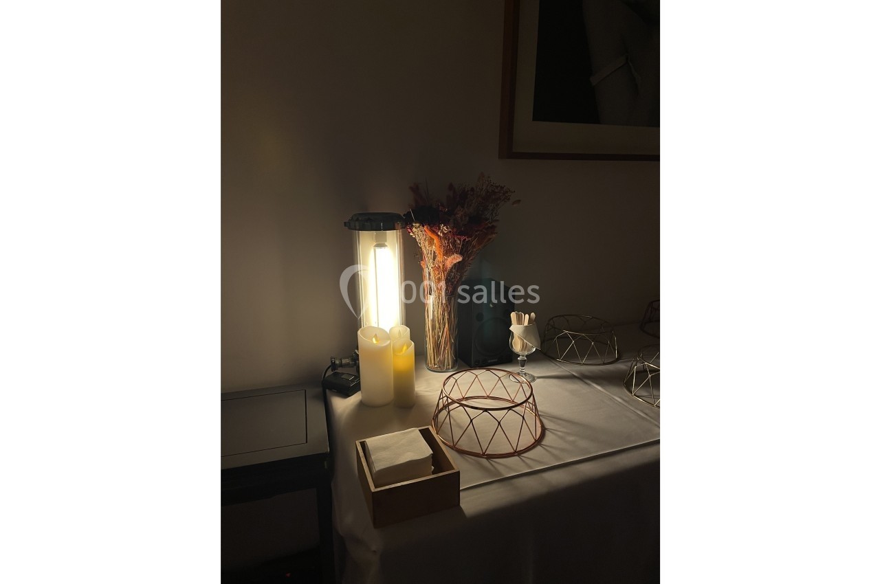 Lampe allumée éclairant une table décorée avec des bougies, un bouquet séché et des objets en métal.