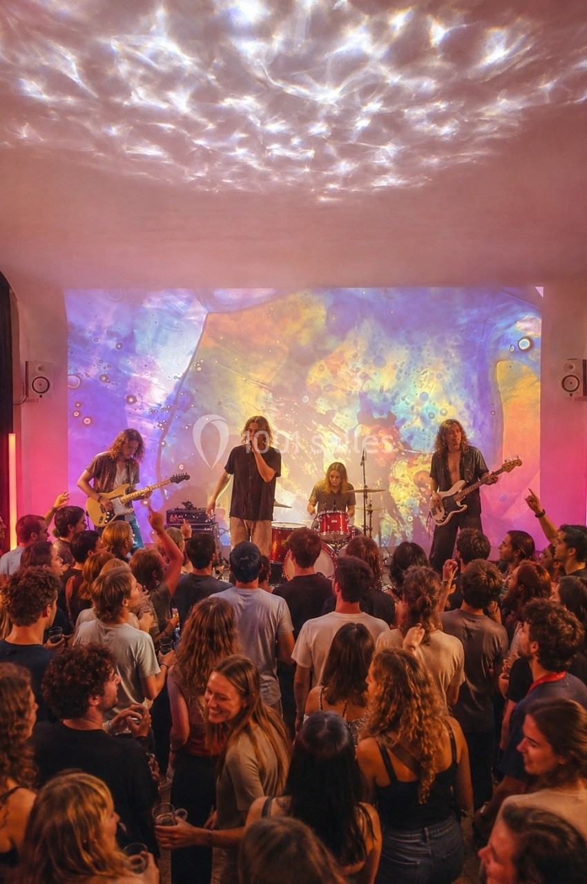 Groupe de musiciens jouant sur scène devant une foule, éclairés par des projections lumineuses colorées.
