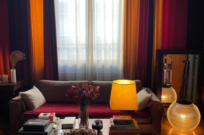 Une chaise en bois et un mannequin près d'une porte ouverte donnant sur un couloir lumineux avec une rambarde en fer forgé.