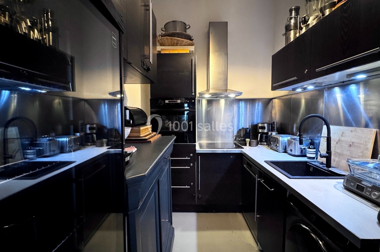 Cuisine moderne avec meubles noirs, plan de travail clair, électroménagers et éclairage intégré sous les placards.