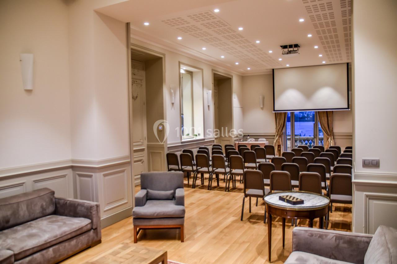 Salle de conférence lumineuse avec rangées de chaises, écran de projection et coin salon aménagé.