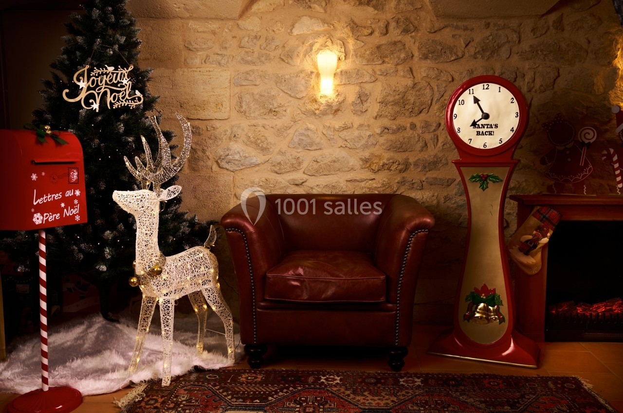 Fauteuil en cuir rouge entouré d'une décoration de Noël avec sapin, renne lumineux, boîte aux lettres et horloge vintage.