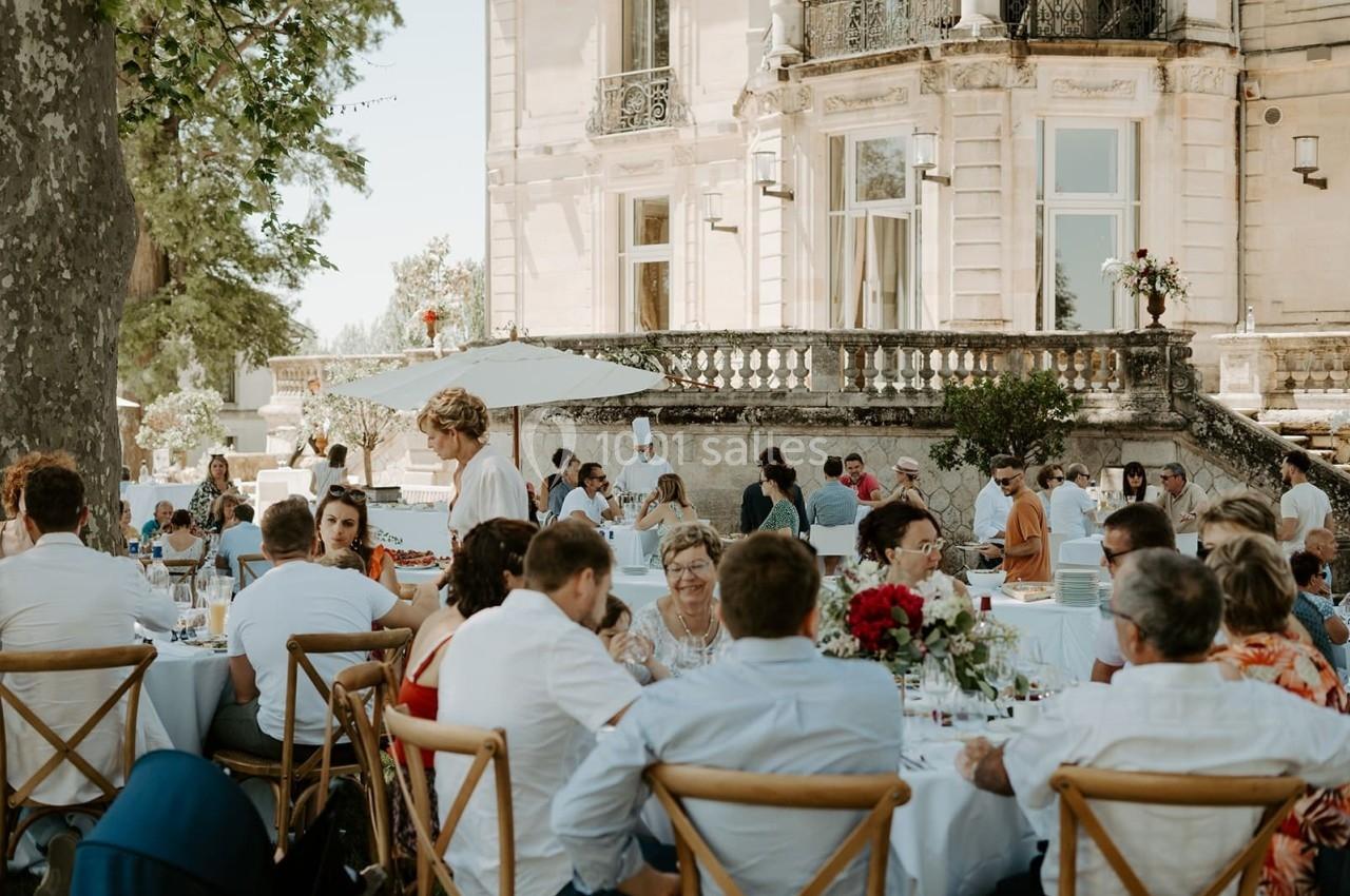 Des convives assis à des tables en plein air devant un bâtiment ancien lors d'un événement festif.