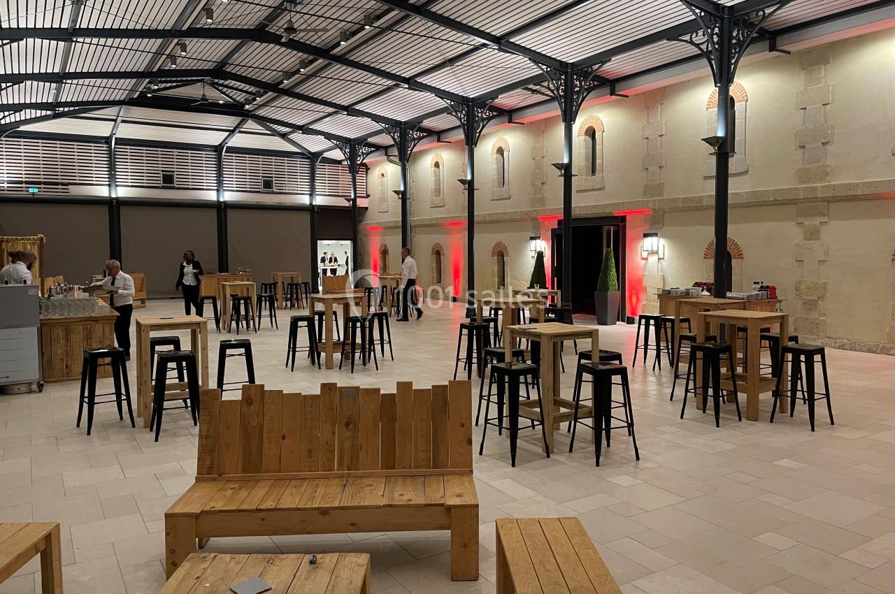 Salle spacieuse avec tables et bancs en bois, éclairage tamisé et murs en pierre, aménagée pour un événement.