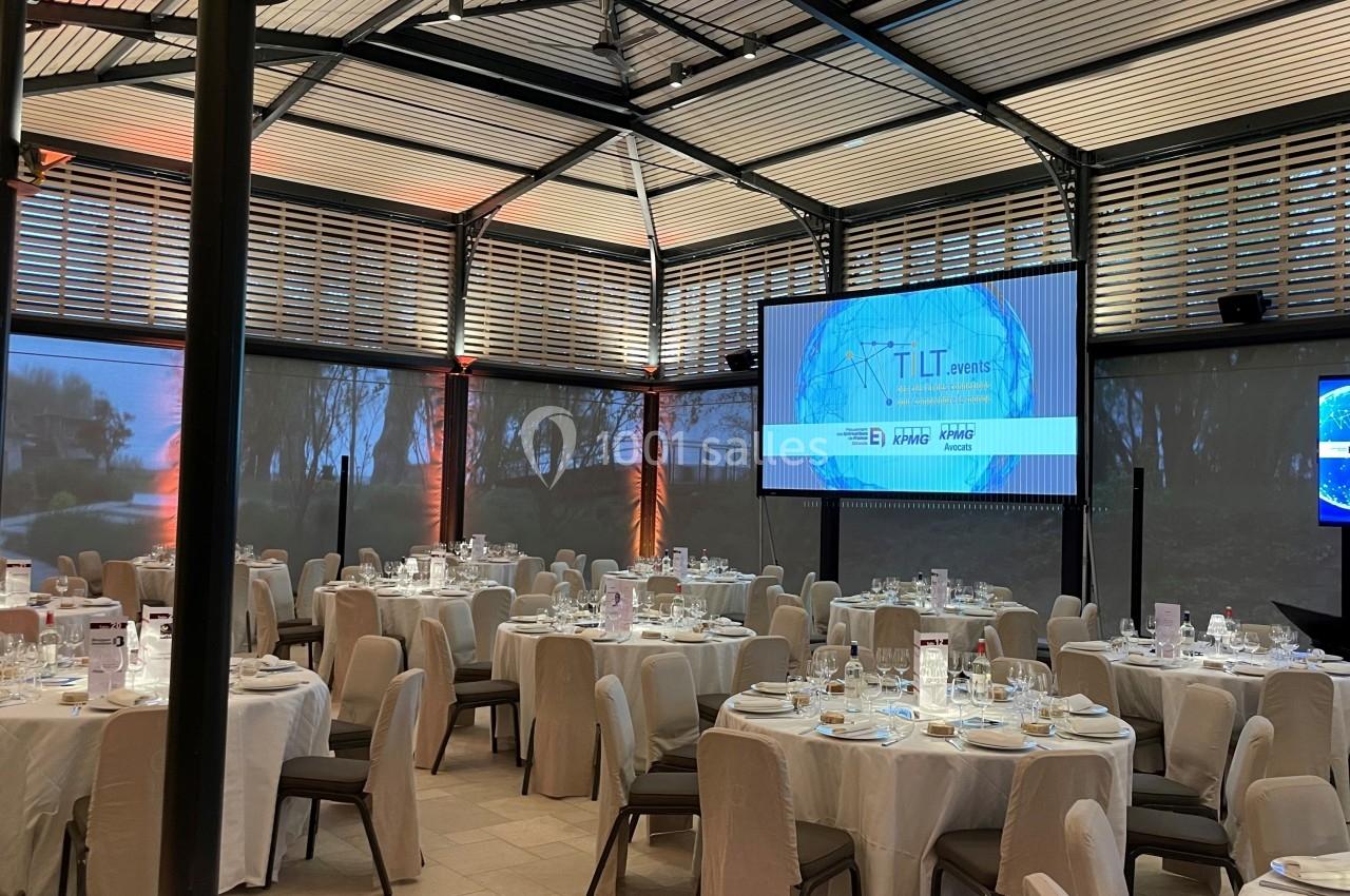 Salle de réception élégante avec tables dressées pour un événement, écran de projection et décor lumineux.