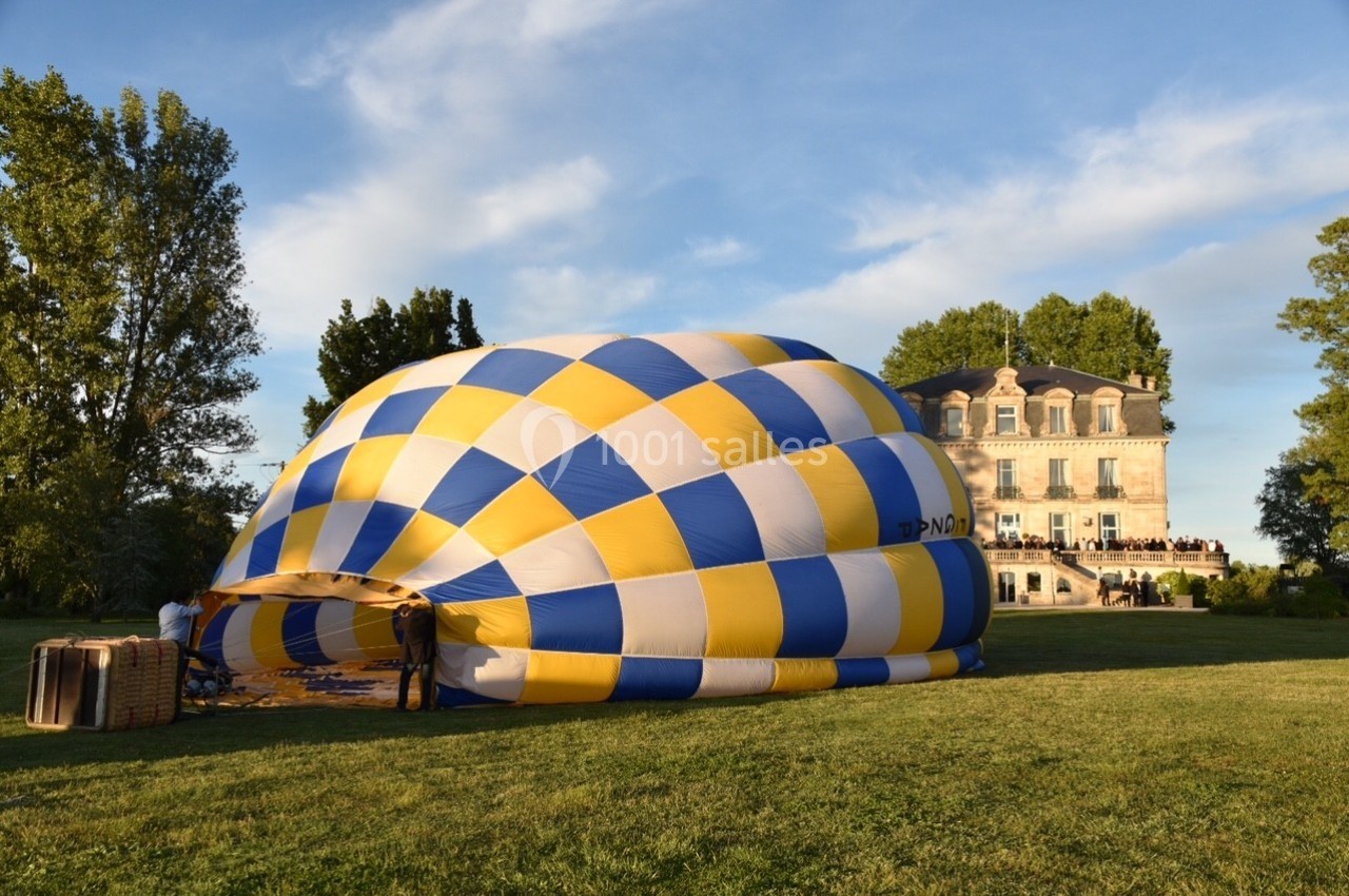 Montgolfière en cours de gonflage sur une pelouse, avec un manoir en arrière-plan et des arbres environnants.