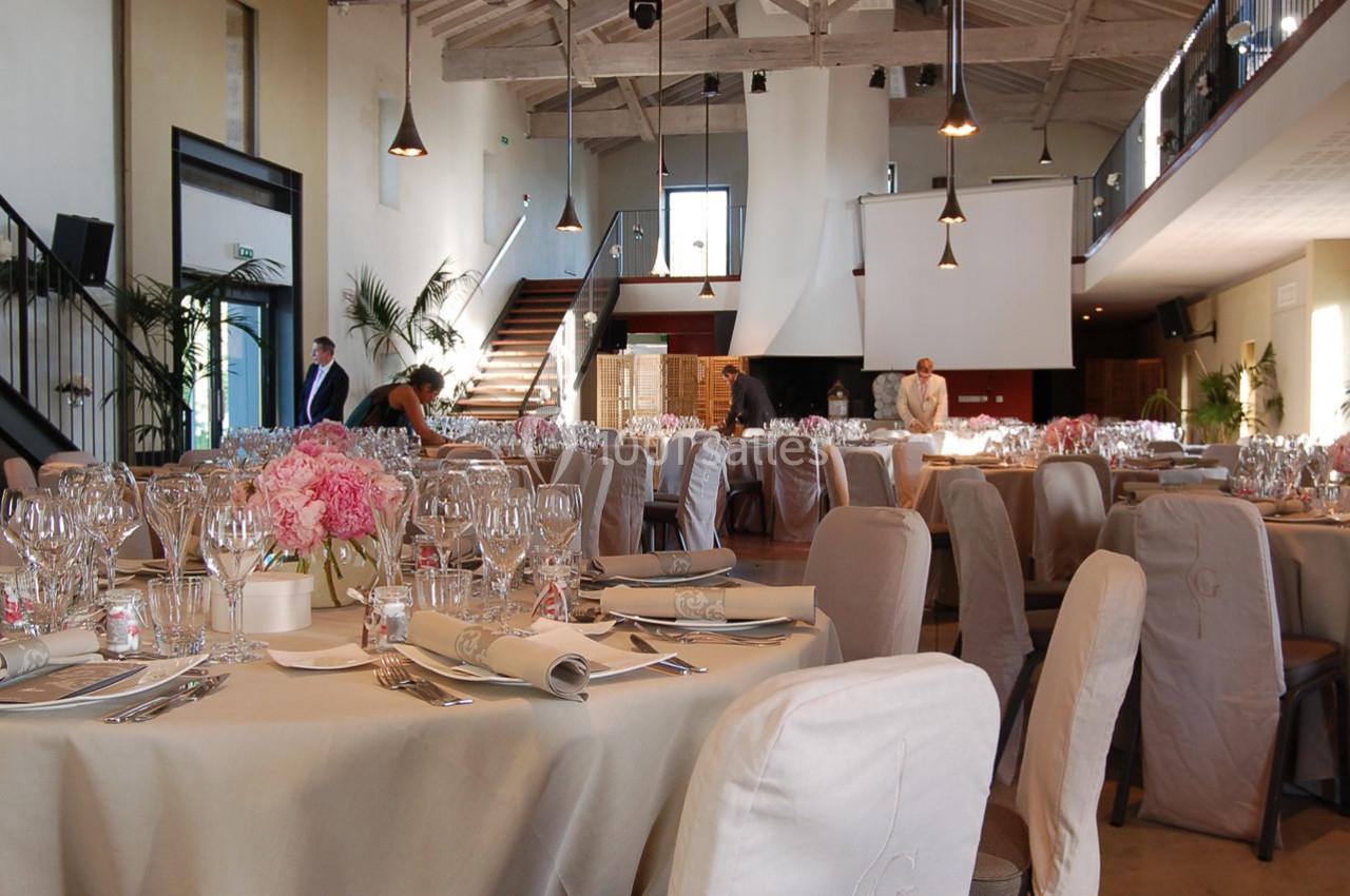 Salle de réception élégamment décorée avec des tables dressées, des chaises houssées et un éclairage chaleureux.
