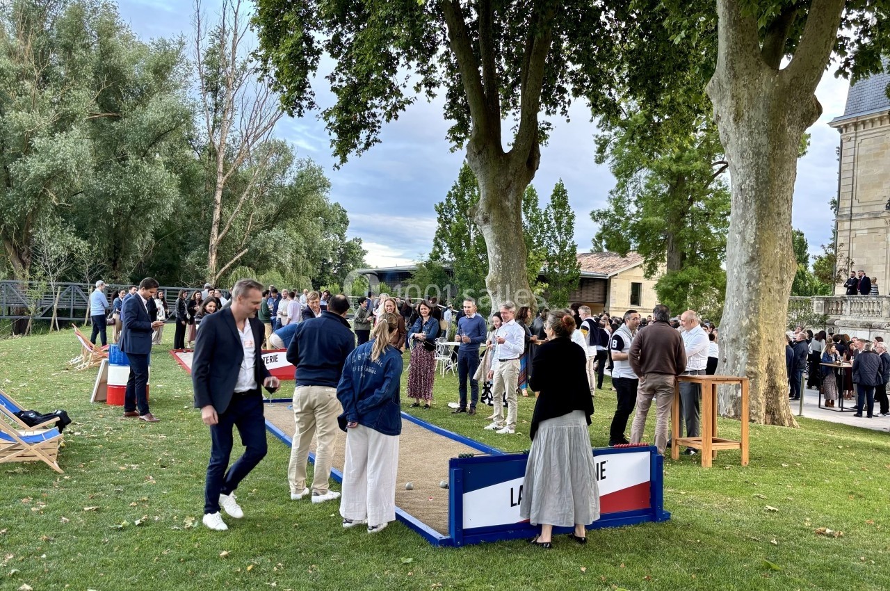 Groupe de personnes rassemblées dans un parc près d'un bâtiment, discutant et jouant à un jeu de pétanque.