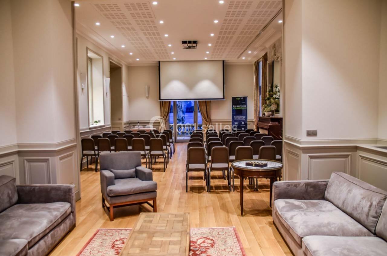 Salle de conférence lumineuse avec rangées de chaises, écran de projection et coin salon en premier plan.