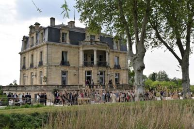 Un groupe de personnes joue au ballon sur une pelouse devant un grand bâtiment ancien sous un ciel dégagé.