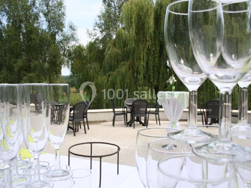 Verres à pied empilés sur une table en extérieur, avec des chaises et des arbres en arrière-plan.