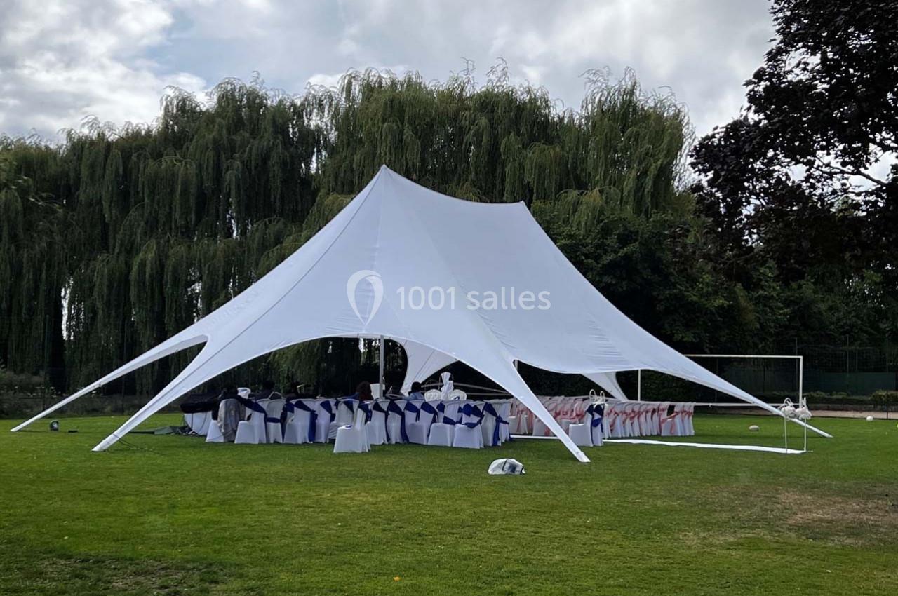 Grande tente blanche montée sur une pelouse, abritant des tables et des chaises décorées pour un événement en plein air.