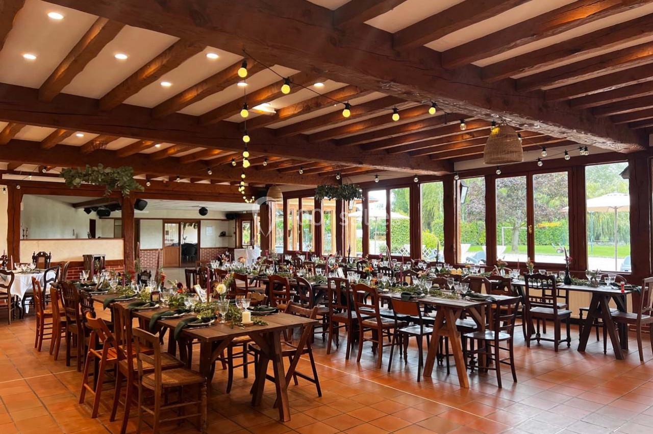 Salle de réception lumineuse avec de grandes tables en bois décorées, poutres apparentes et vue sur un jardin verdoyant.