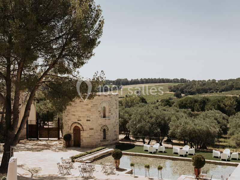 Cour extérieure avec piscine, chaises longues blanches, tables en fer forgé, entourée d'arbres et de vignobles sous un ciel…