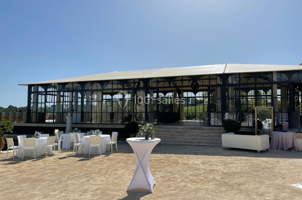 Vue d'une grande verrière avec des tables dressées en extérieur sur une terrasse ensoleillée.
