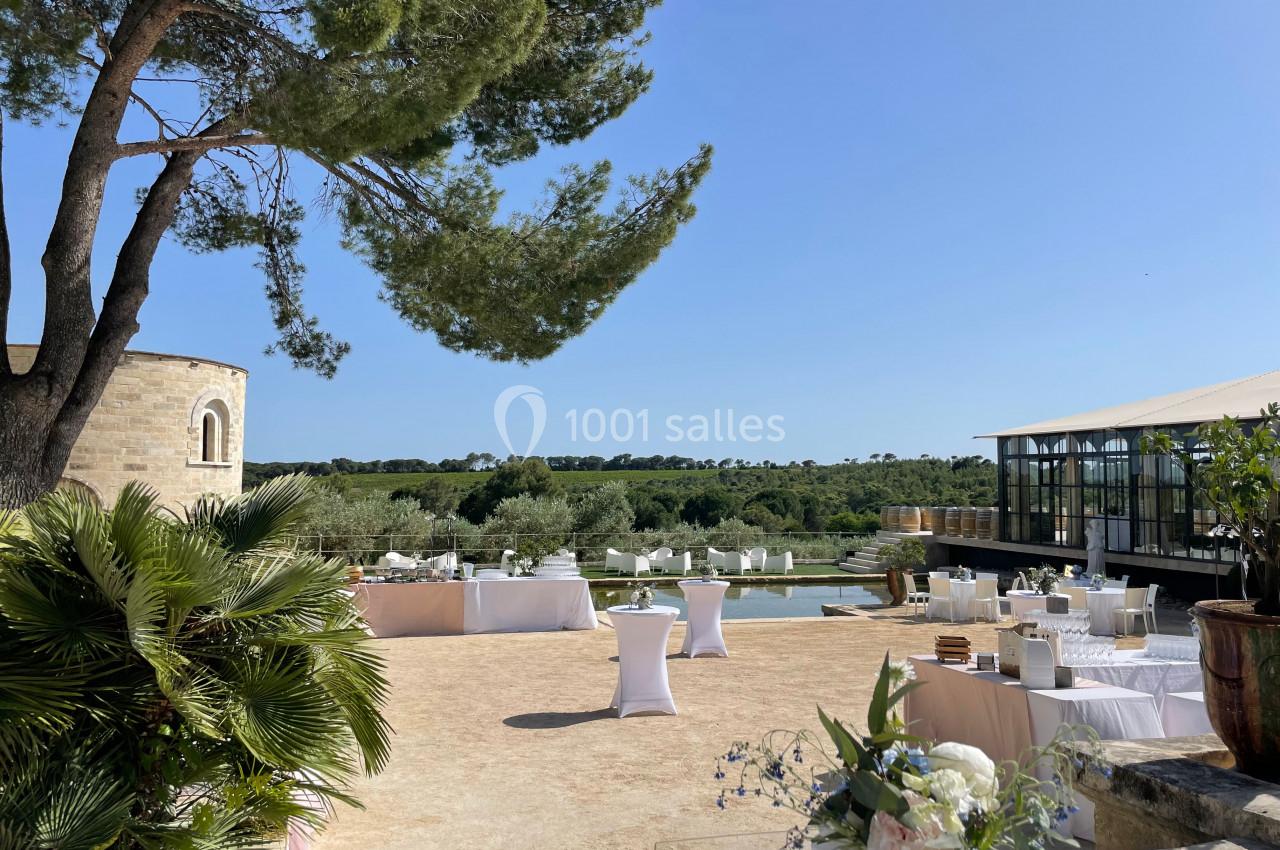 Terrasse ensoleillée avec tables dressées, vue sur un paysage verdoyant, une chapelle et une structure moderne.
