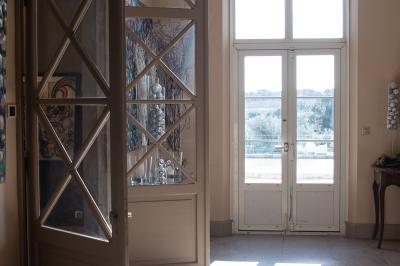 Vue d'une pièce lumineuse avec sol en carreaux anciens, mobilier classique et une chambre attenante avec lit à baldaquin.