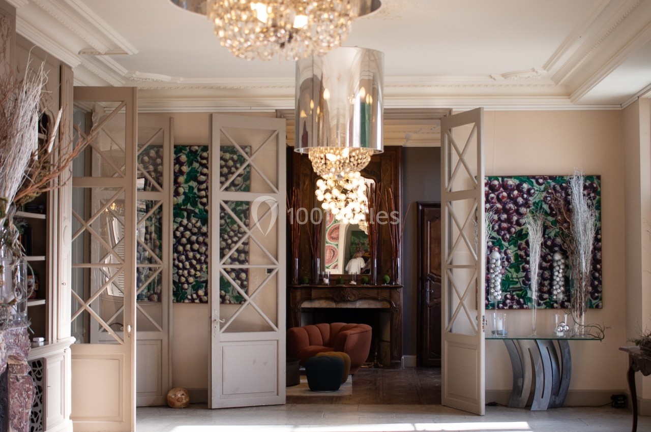 Intérieur lumineux avec lustres modernes, portes vitrées ouvertes et fauteuil visible dans une pièce adjacente.