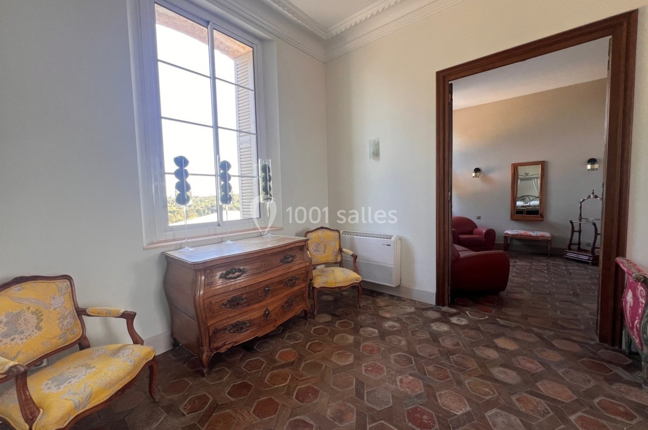 Pièce lumineuse avec sol en carreaux anciens, commode en bois, fauteuils jaunes et vue sur un salon adjacent.