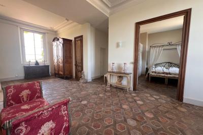 Vue d'une pièce lumineuse avec sol en carreaux anciens, mobilier classique et une chambre attenante avec lit à baldaquin.