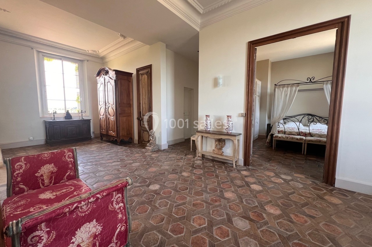 Vue d'une pièce lumineuse avec sol en carreaux anciens, mobilier classique et une chambre attenante avec lit à baldaquin.