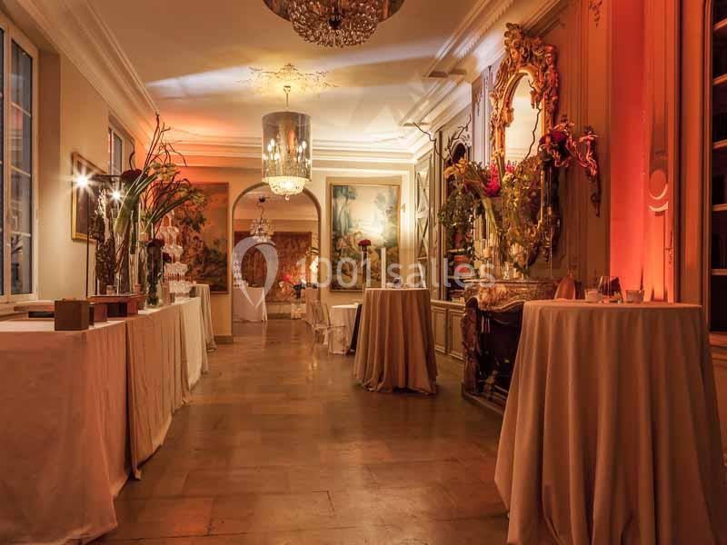 Salle élégante avec tables drapées, éclairage chaleureux, miroirs dorés et décorations florales.