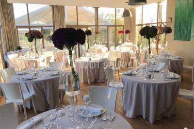 Tour en pierre entourée de végétation, avec bassin d'eau, chaises et tables en métal sur une terrasse ensoleillée.