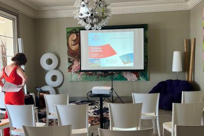 Tour en pierre entourée de végétation, avec bassin d'eau, chaises et tables en métal sur une terrasse ensoleillée.