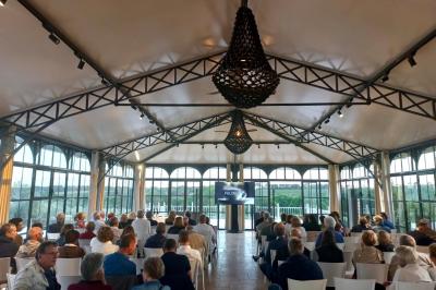 Tour en pierre entourée de végétation, avec bassin d'eau, chaises et tables en métal sur une terrasse ensoleillée.