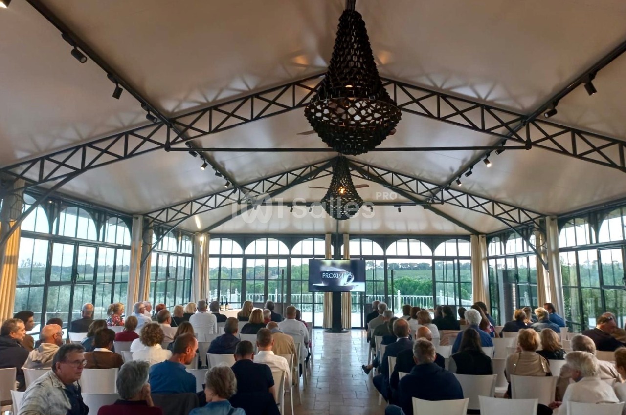 Salle lumineuse avec des invités assis, regardant une présentation sur un écran sous une structure en métal et toile.