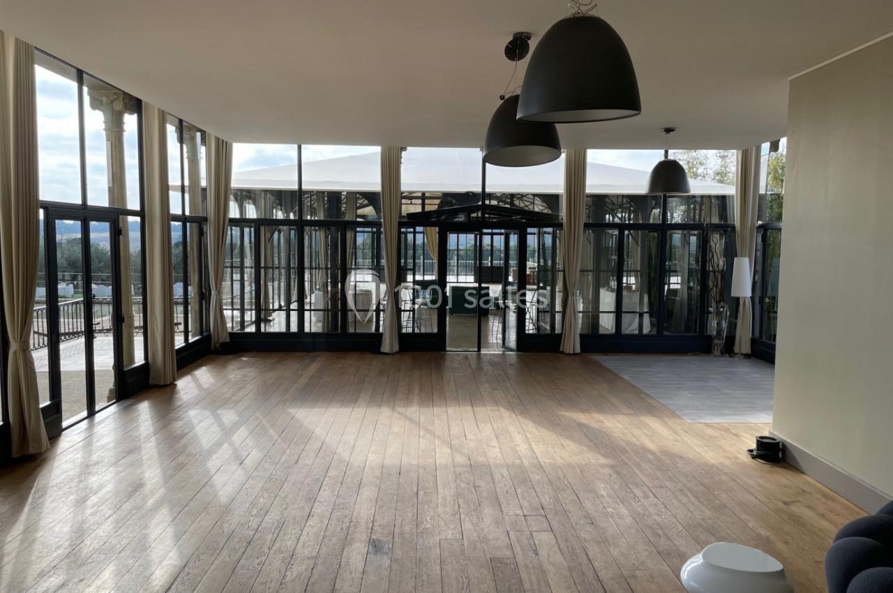 Salle lumineuse avec parquet en bois, grandes baies vitrées donnant sur une terrasse et un espace extérieur couvert.