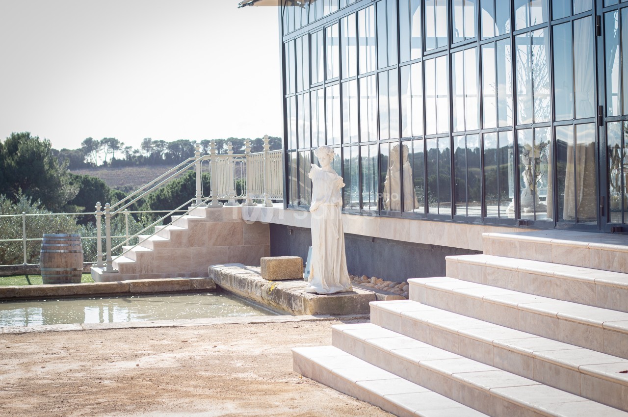 Statue blanche près d'un bassin, devant un bâtiment vitré entouré d'escaliers et d'un paysage naturel.