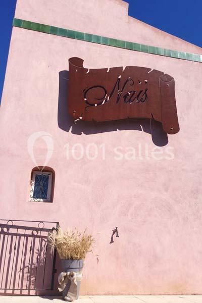 Location salle Rognes (Bouches-du-Rhône) - Domaine Naïs #12 Façade rose avec une enseigne métallique ’Naïs’, une petite fenêtre, un robinet mural et un pot de plantes sèches.
