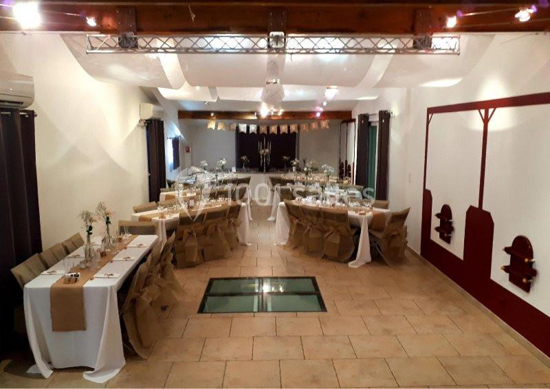 Location salle Rognes (Bouches-du-Rhône) - Domaine Naïs #8 Salle de réception décorée avec des tables dressées, nappes blanches et chaises couvertes, sous un plafond en poutres…