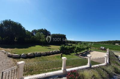 Miniature Location salle Rognes (Bouches-du-Rhône) - Domaine Naïs #3 Terrasse en pierre avec des tonneaux en bois, vue sur un paysage verdoyant et une clôture en fer forgé.