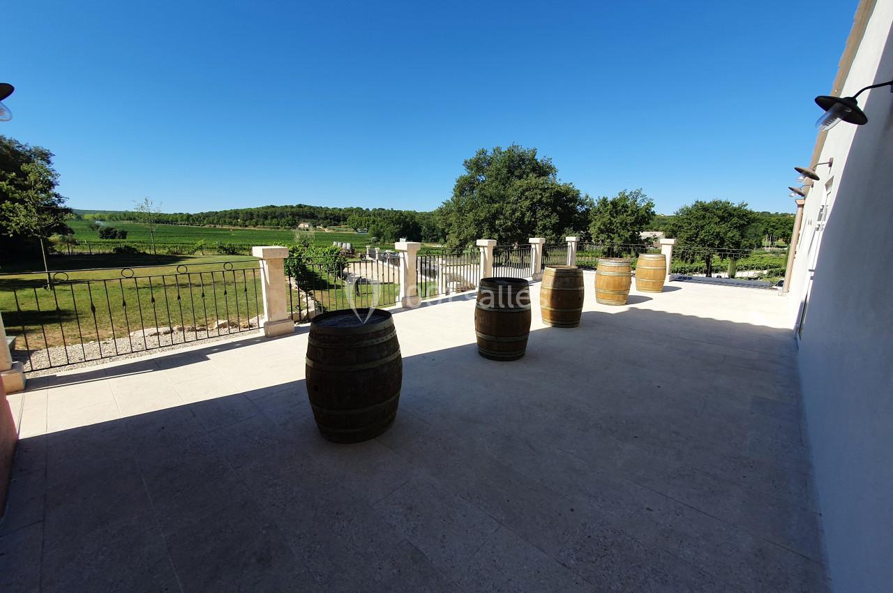 Location salle Rognes (Bouches-du-Rhône) - Domaine Naïs #24 Terrasse en pierre avec des tonneaux en bois, vue sur un paysage verdoyant et une clôture en fer forgé.