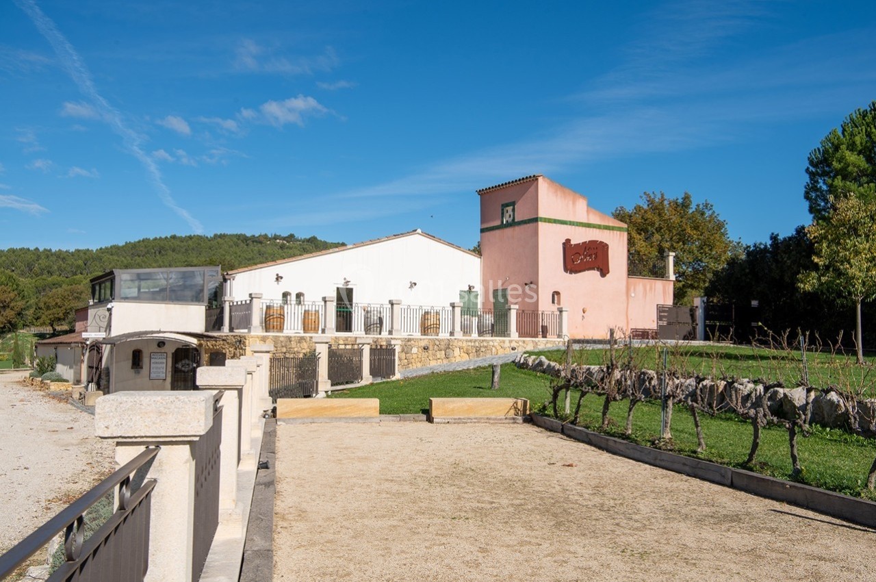 Bâtiment aux façades claires entouré de vignes et d'espaces verts sous un ciel bleu dégagé.