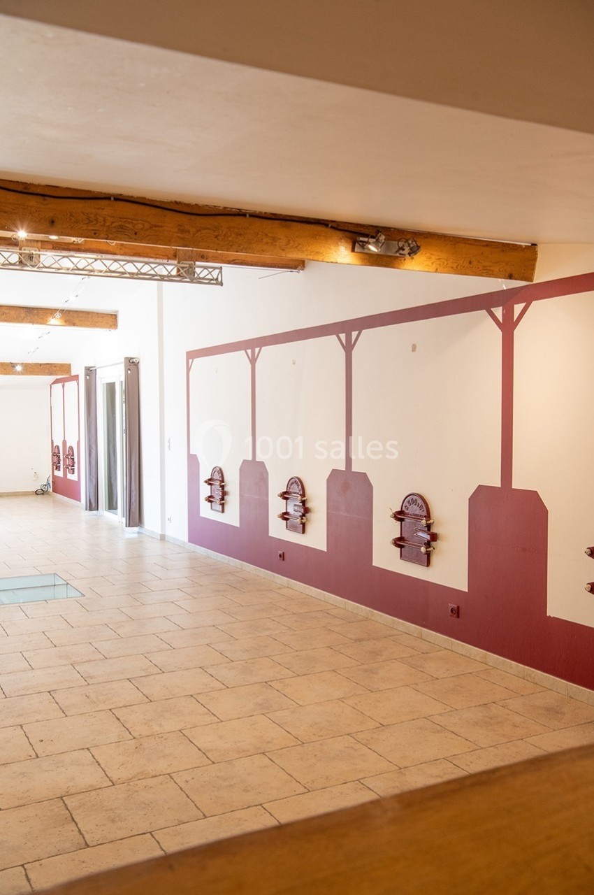 Salle lumineuse avec murs décorés de motifs rouges, poutres apparentes et sol en carrelage clair.