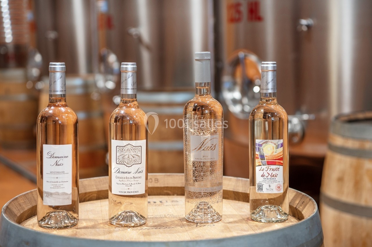 Location salle Rognes (Bouches-du-Rhône) - Domaine Naïs #9 Quatre bouteilles de vin rosé posées sur un tonneau en bois, avec des cuves en acier en arrière-plan.
