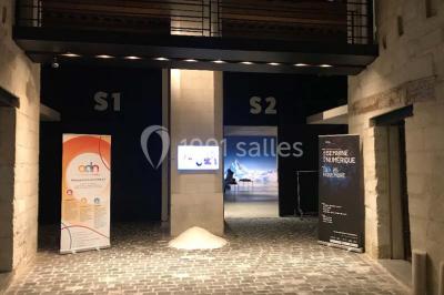 Salle d'exposition avec des œuvres accrochées aux murs, tables hautes et projection lumineuse ’Réseau AMA’.