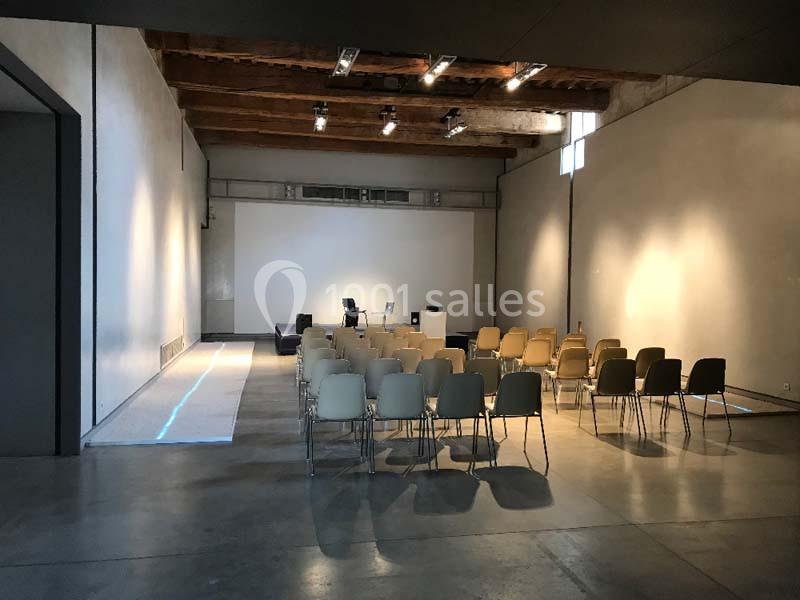 Salle vide avec des rangées de chaises beige et noires, un projecteur et un pupitre devant un mur blanc.