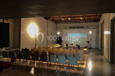 Salle d'exposition avec des œuvres accrochées aux murs, tables hautes et projection lumineuse ’Réseau AMA’.