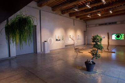 Salle d'exposition avec des œuvres accrochées aux murs, tables hautes et projection lumineuse ’Réseau AMA’.