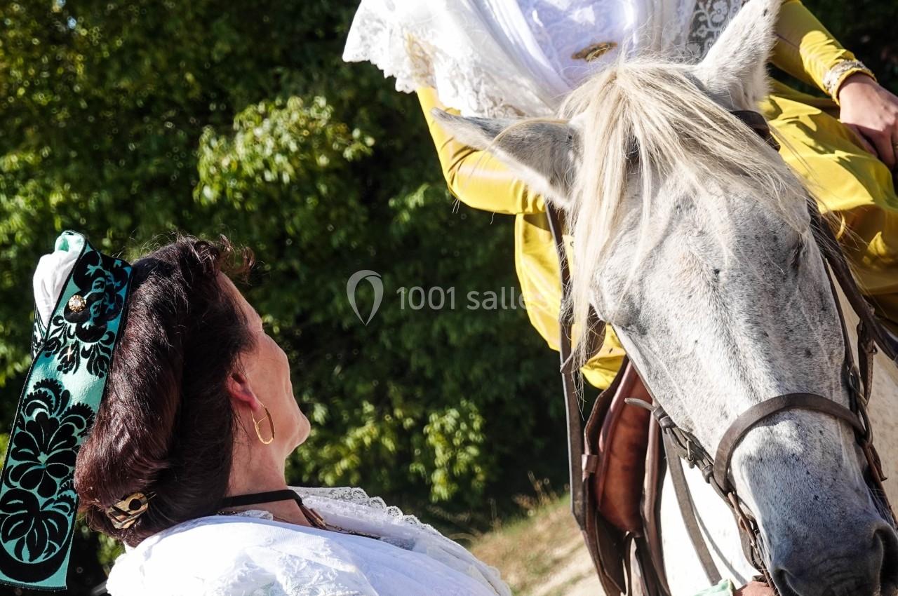 Deux femmes en tenue traditionnelle, l'une à cheval et l'autre à pied, discutent dans un cadre extérieur verdoyant.