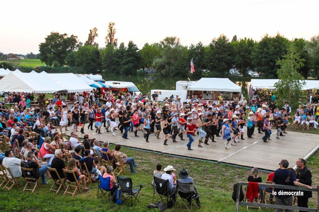 Groupe de personnes dansant en ligne sur une scène en plein air lors d'un événement festif près d'un plan d'eau.